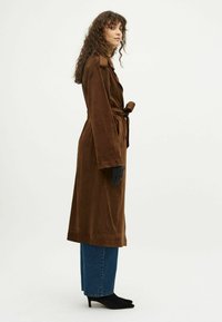 Bruine suedewinterjas met een gestrikte taille, zijzakken en schouderepauletten. Draag het over blauwe rechte spijkerbroeken en zwarte enkelboots met hak.