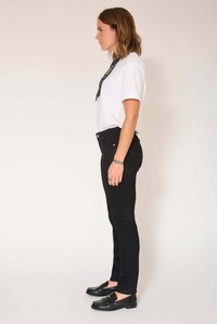Jean skinny noir taille haute avec cinq poches, fermeture avant par bouton, porté avec un t-shirt blanc et des mocassins noirs.