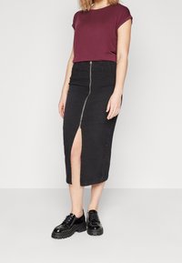 Černá džínová midi sukně se zipem vpředu a rozparkem na boku, doplněná vínově červeným krátkým tričkem a černými botami na platformě.