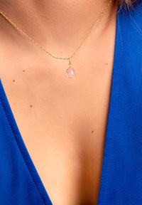 Collana in oro con pendente a forma di pera in pietra rosa sfacettata. La catena è delicata e ha una leggera lucentezza.