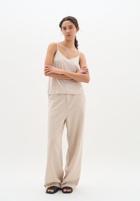 Camisole di seta beige con spalline sottili, abbinato a pantaloni larghi beige chiaro. Sandali neri a scivolo completano l'outfit. Design minimalista.