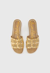 Kulta slip-on sandaalit, joissa on teksturoitu kudottu pohja, koristeltu monimutkaisilla pitsi- ja jalokivimäisillä yksityiskohdilla. Litteä muotoilu avonaisella varpaalla.