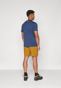 Navy blue short-sleeve t-shirt with round neck, paired with mustard yellow shorts. Model wears black hiking shoes with gray accents.