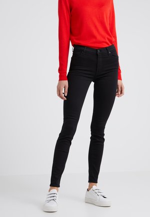Črne jeans hlače slim fit kroja, narejene iz jeansa. V kombinaciji z rdečo srajco z dolgimi rokavi in belimi supergami.