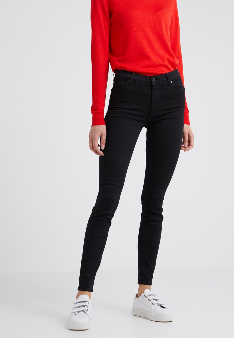 Jean noir avec une coupe slim, fabriqué en tissu denim. Associé à une chemise à manches longues rouge et des baskets blanches.