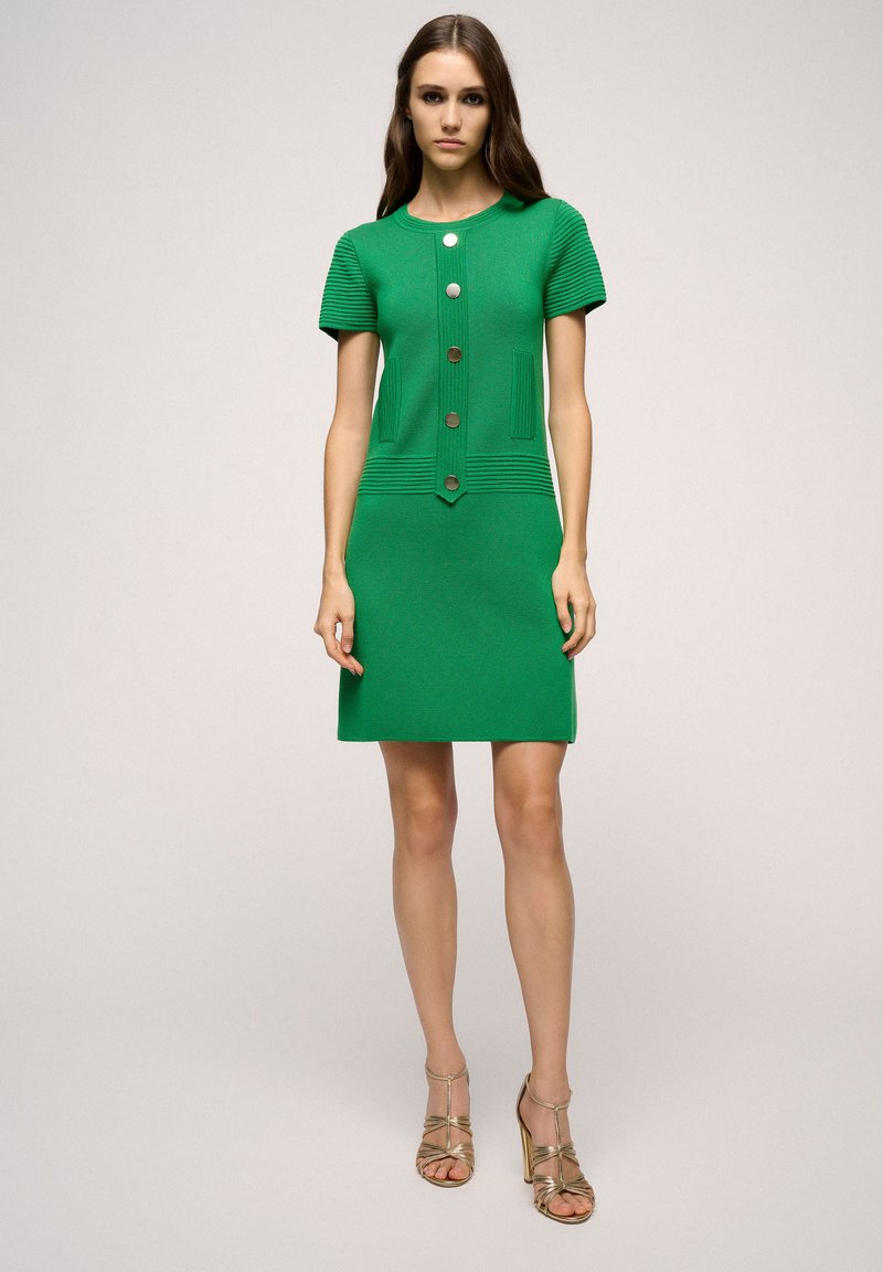 Abito verde a maglia con maniche corte, corpetto textured e grandi bottoni. Silhouette aderente con orlo dritto e tasche decorative.