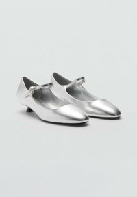 Ballerine metalliche argento con cinturino Mary Jane e tacco basso. Texture liscia, design a punta e stile minimalista semplice.
