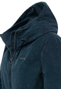 Mørkeblå fløjlsjakke med høj krave, lynlåslukning foran og metalbeslag. Blød tekstur og fremhævet med et logo-patch på siden.