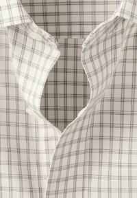 Chemise blanche à boutons avec un motif à fines carreaux noirs, partiellement déboutonnée au niveau du col.