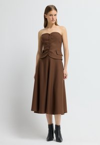 Hněd dress bez ramínek s texturovanou tkaninou, má knoflíkovou přední část a rozšířenou sukni. V kombinaci s černými kotníkovými botami.