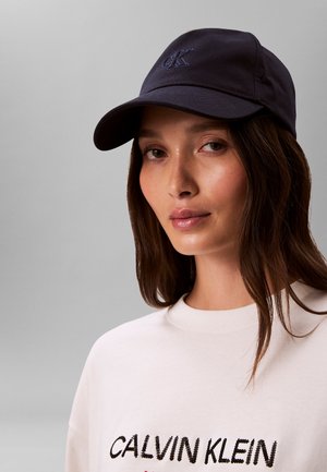 Granatowa czapka z daszkiem z wyhaftowanym logo "CK", z zakrzywionym daszkiem i gładką fakturą materiału. Połączona z białą bluzą.