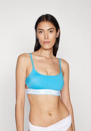 Een blauwe, aansluitende beha met dunne bandjes en een witte elastische band met het Calvin Klein-logo. Gladde textuur en naadloos ontwerp.