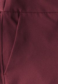 Tissu bordeaux au toucher lisse, présentant un design plié et une couture visible. Aucun motif ni accessoire présent.