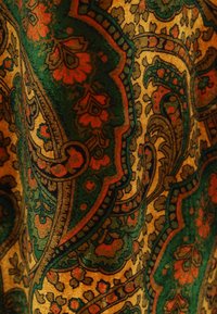 Tessuto con un intricato motivo paisley che presenta disegni floreali in rosso, verde e oro su uno sfondo testurizzato dorato.