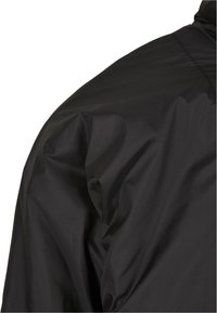 Black waterproof jacket featuring a smooth, matte finish, structured shoulders, and visible seams. Designed for durability and protection.