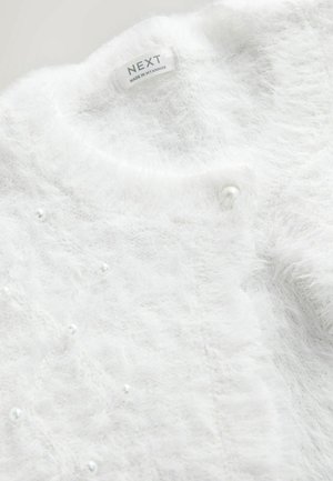 Weißer flauschiger Cardigan mit weicher Textur, rundem Hals, perlenähnlichen Akzenten und einem Etikett mit der Aufschrift "NEXT, hergestellt in Myanmar."