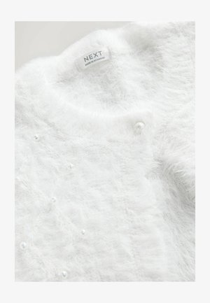 Cardigan alb pufos cu textură moale, cu guler rotund, accente asemănătoare cu perlele și o etichetă pe care scrie „NEXT, fabricat în Myanmar”.