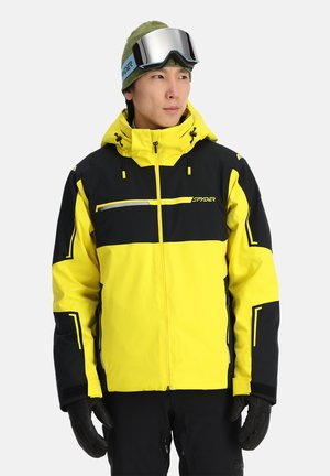 Yellow and black ski jacket featuring a zippered chest pocket, adjustable hood, and elastic cuffs. Worn with black gloves and goggles.