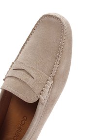Beige suède loafers met een gepolsterde bovenkant, gestikte accenten en een opvallend moccasinstijl ontwerp. Glad, textuur oppervlak.
