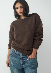 Brown knitted sweater with a crew neckline, textured fabric, and ribbed cuffs, paired with light blue denim jeans.