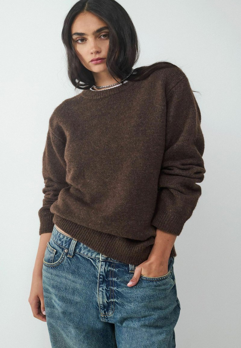 Brown knitted sweater with a crew neckline, textured fabric, and ribbed cuffs, paired with light blue denim jeans.