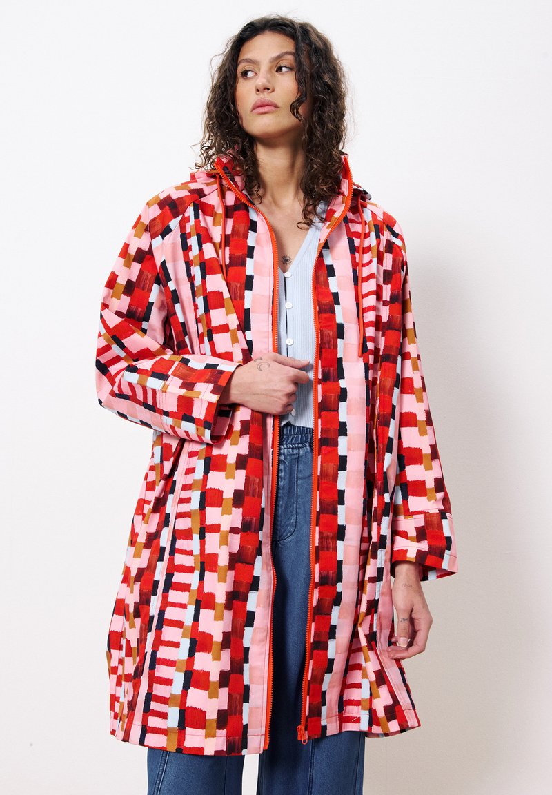 Colorful, patterned raincoat featuring a mix of reds, pinks, and browns. Includes a hood, front zipper, and loose-fitting sleeves.