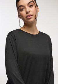 Maglietta nera a maniche lunghe in tessuto morbido con un fitting rilassato, dotata di scollatura rotonda e drappeggi sottili sulle spalle.