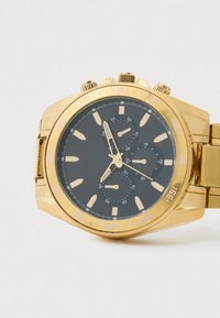 Chronograph-Uhr in Goldoptik mit schwarzem Zifferblatt, großen Stundenmarkierungen, Nebenzifferblättern und Metallarmband. Verfügt über eine Tachymeter-Lünette.