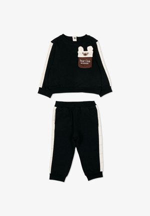 Survêtement pour tout-petit noir avec des bandes latérales crème, comprenant une poche avec écusson "Bear Club" affichant un visage d'ours sur le sweat-shirt.