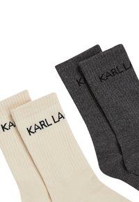 Puuvillased sokid helesbežis ja tumastes hallis, ribakujundusega ja musta logoga, üksteise peale virna pandud.