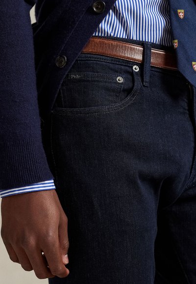 Mørkeblå denimjeans har en rett passform, kontrasterende mansjetter med lyseblå og hvite striper på skjorten, og et brunt lærbelte med metalspenne.