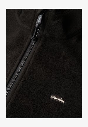 Veste en polaire noire avec fermeture éclair intégrale, dotée d'une surface texturée, d'un petit logo brodé et d'une tirette de fermeture robuste.