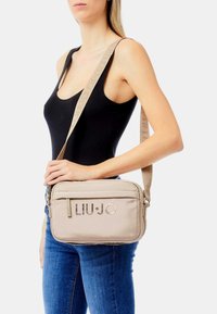 Borsa a tracolla beige LIU JO con finitura testurizzata, dotata di un compartimento principale, dettagli con logo e una tracolla regolabile.