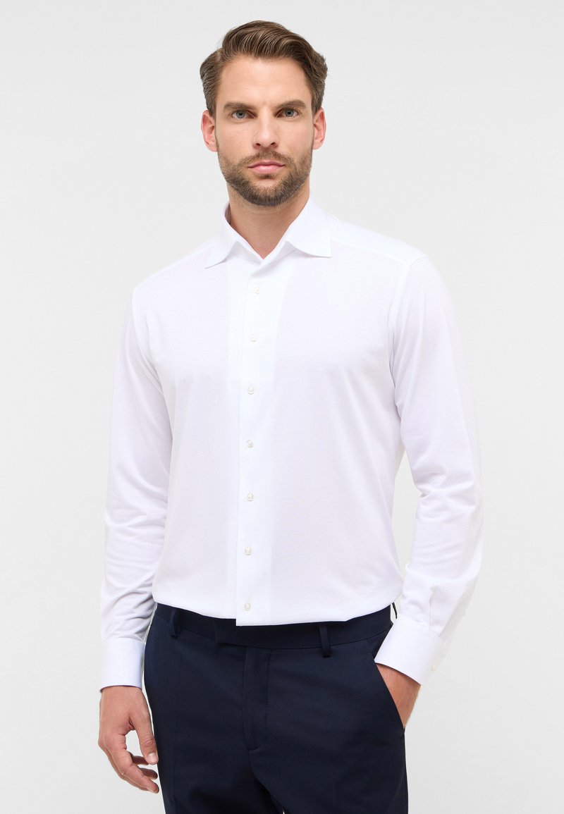 Witte langemouwenshirt met een klassieke kraag, knoopsluiting en subtiele textuur. Gecombineerd met donkerblauwe broek.