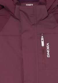 Bordo jakna z navpično zadrgo na prsnem žepu, označena z "VIKING", z napisom "TOASTY" nad žepom blizu ovratnika.