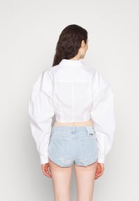 Witte crop top met opstaande mouwen en een kraag, gecombineerd met lichtblauwe verouderde denimshorts met achterzakken en een merklabel.