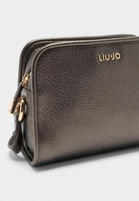 Sac en cuir texturé gris foncé avec un logo doré "LIU JO", fermeture éclair et une sangle détachable pour le porter.