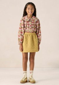Multicolored floral long-sleeve shirt with ruffled collar, paired with a textured yellow quilted skirt. Features striped socks and beige sneakers.