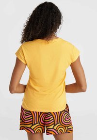 T-shirt di cotone gialla con maniche corte, abbinata a pantaloni corti multicolori con motivi a spirale in rosa, arancione e nero.