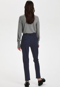 Pelēka garām piedurknēm blūze un tumši zili šorti ar šauru piegriezumu. Šortiem ir sānu kabatas un sarullētas piedurknes. Redzami melni platforma apavi.