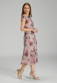 Robe midi florale dans des nuances de rose et de gris, avec des manches flottantes, un corsage ajusté et une jupe fluide avec un léger éclat. Sandales à talons hauts argentées.