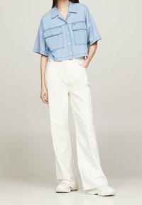 Cropped light blue denim shirt with two front pockets, paired with wide white cotton pants and white sneakers. Minimalist design and loose fit.