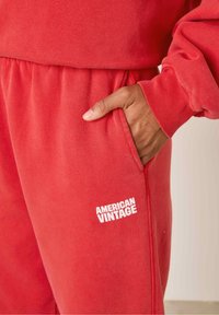 Punased puuvillased dressipüksid elastse vöökoha ja küljetaskutega, alumise vasaku jala peal valge "AMERICAN VINTAGE" logo.