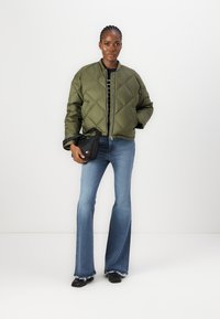 Veste bomber matelassée vert olive avec fermeture éclair sur le devant, portée sur un haut à rayures noir et blanc. Assortie à un jean bleu évasé et un sac noir.