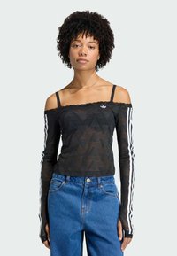 Top negro de hombros descubiertos con borde de encaje, con mangas largas con rayas blancas y un patrón geométrico. Combinado con vaqueros azules de talle alto.