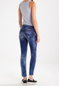 Úzké džíny ve středně modrém denimu s vybledlými detaily a sepranými prvky. Nosit s šedým tílkem a černými botami na klínku.