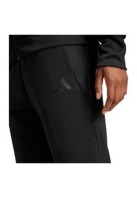 Schwarze Sporthosen mit texturierter Oberfläche, die ein dezentes, geprägtes Logo an der Hüfte und ein schmales Design aufweisen.