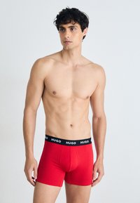 Rote Boxershorts aus Baumwolle mit einem schwarzen elastischen Bund, der das "HUGO"-Logo trägt. Angenehme Passform und glatte Textur.