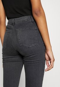 Mörkgrå jeans med hög midja tillverkade av denim, med böjda bakfickor och en avsmalnande benform. Slät textur med liten slitageeffekt.
