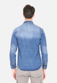 Camicia di denim azzurra chiara, con colletto a punta, maniche lunghe e orlo curvo. Tessuto invecchiato con una superficie liscia.